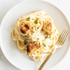 A white plate with fettuccine alfredo topped with spiedini.