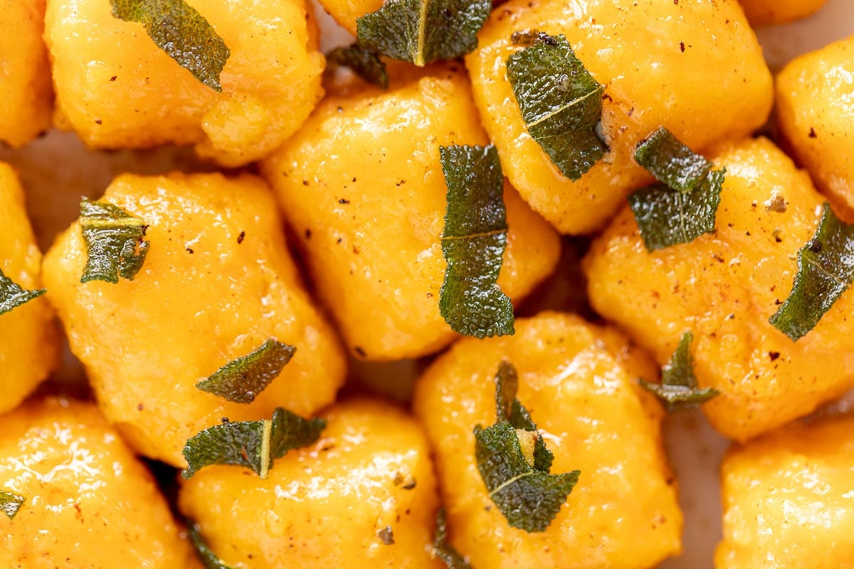 A close up of sweet potato gnocchi with sage leaves on a plate.