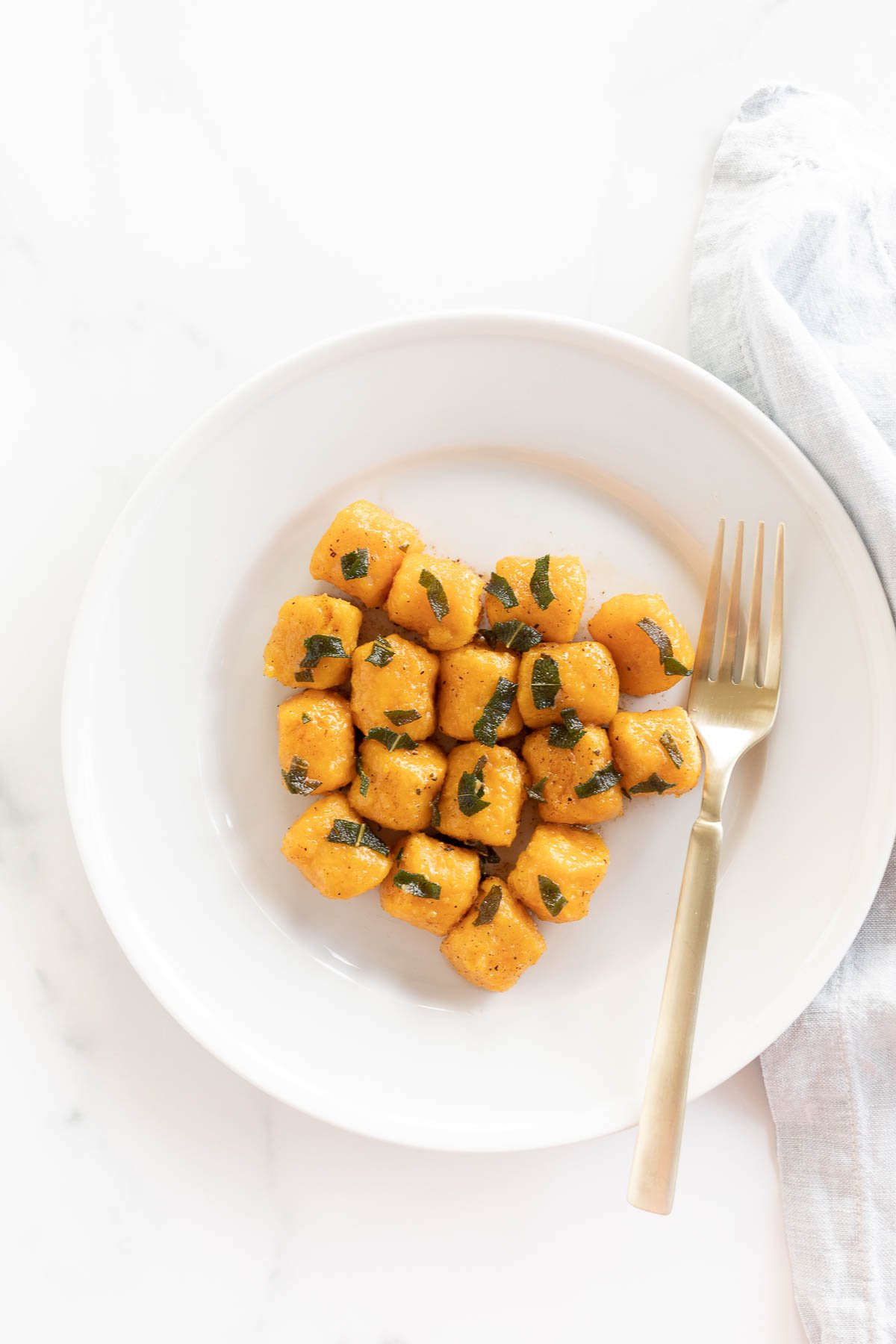 Sweet potato gnocchi beautifully presented on a white plate, delicately flattened with a fork.