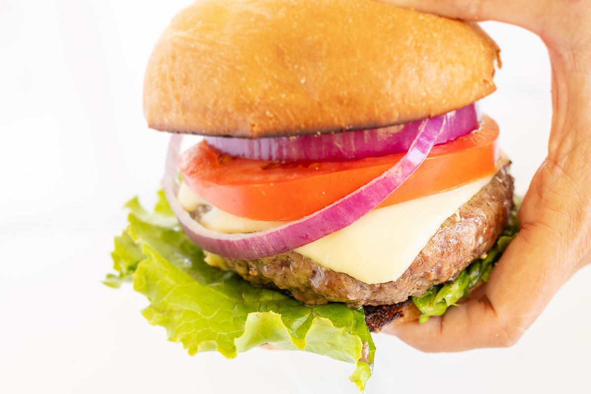 A burger stacked with toppings and a toasted burger bun, held in a hand