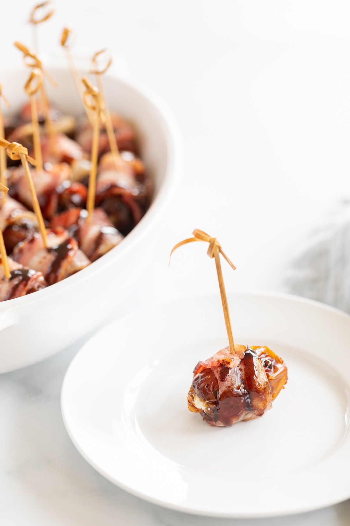 A fig wrapped in bacon on a white plate for a Thanksgiving appetizer.