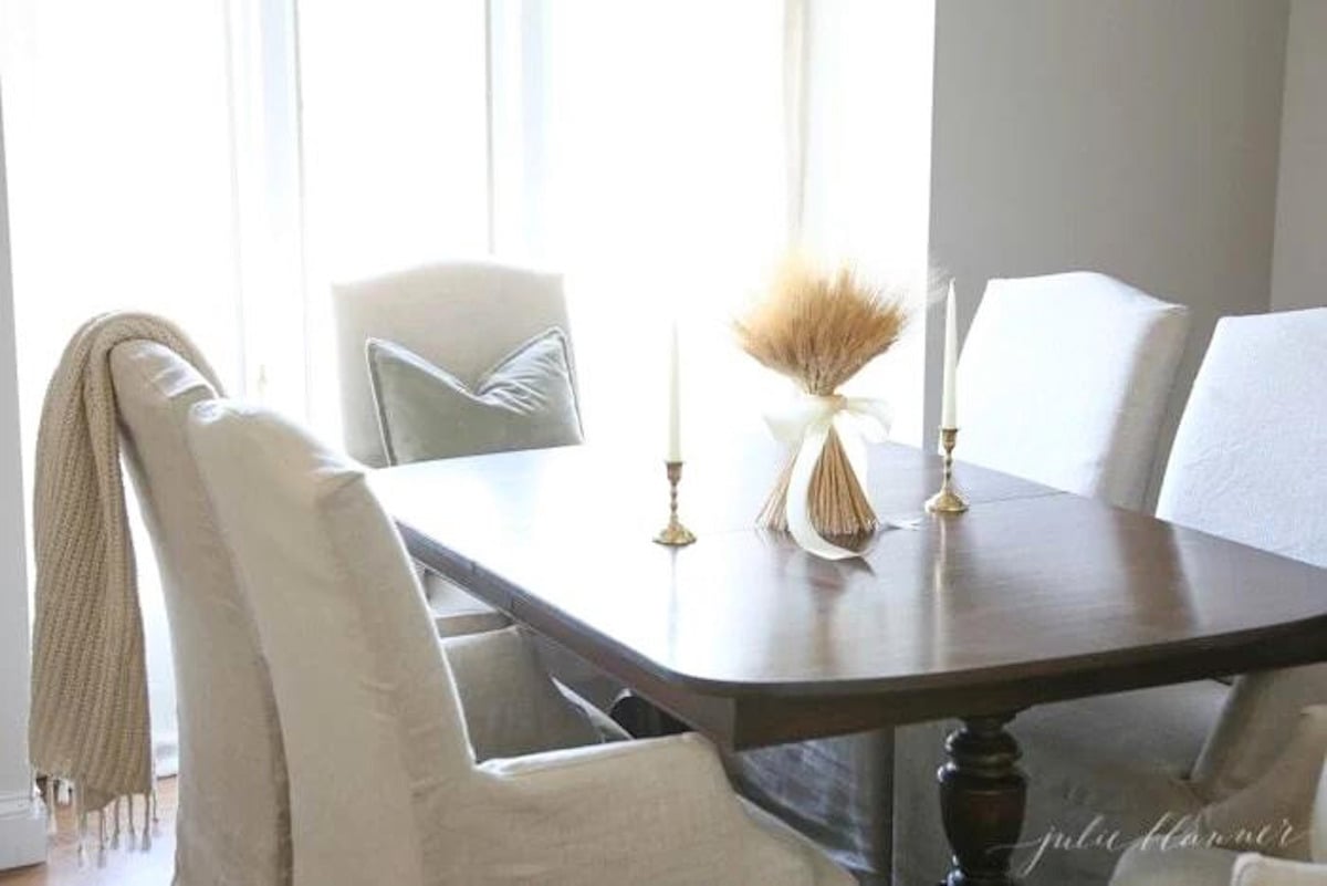 A dining room with a white table and chairs featuring Thanksgiving table decor.
