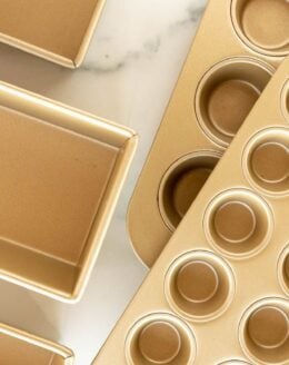 A variety of gold cake pans, loaf pans and muffin baking pan sizes laid out on a marble surface.