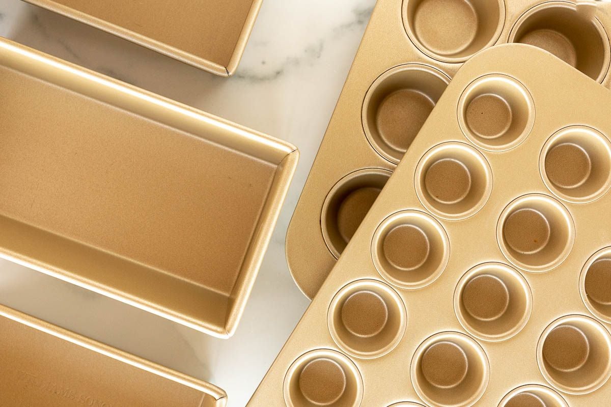 A variety of gold cake pans, loaf pans and muffin baking pan sizes laid out on a marble surface.