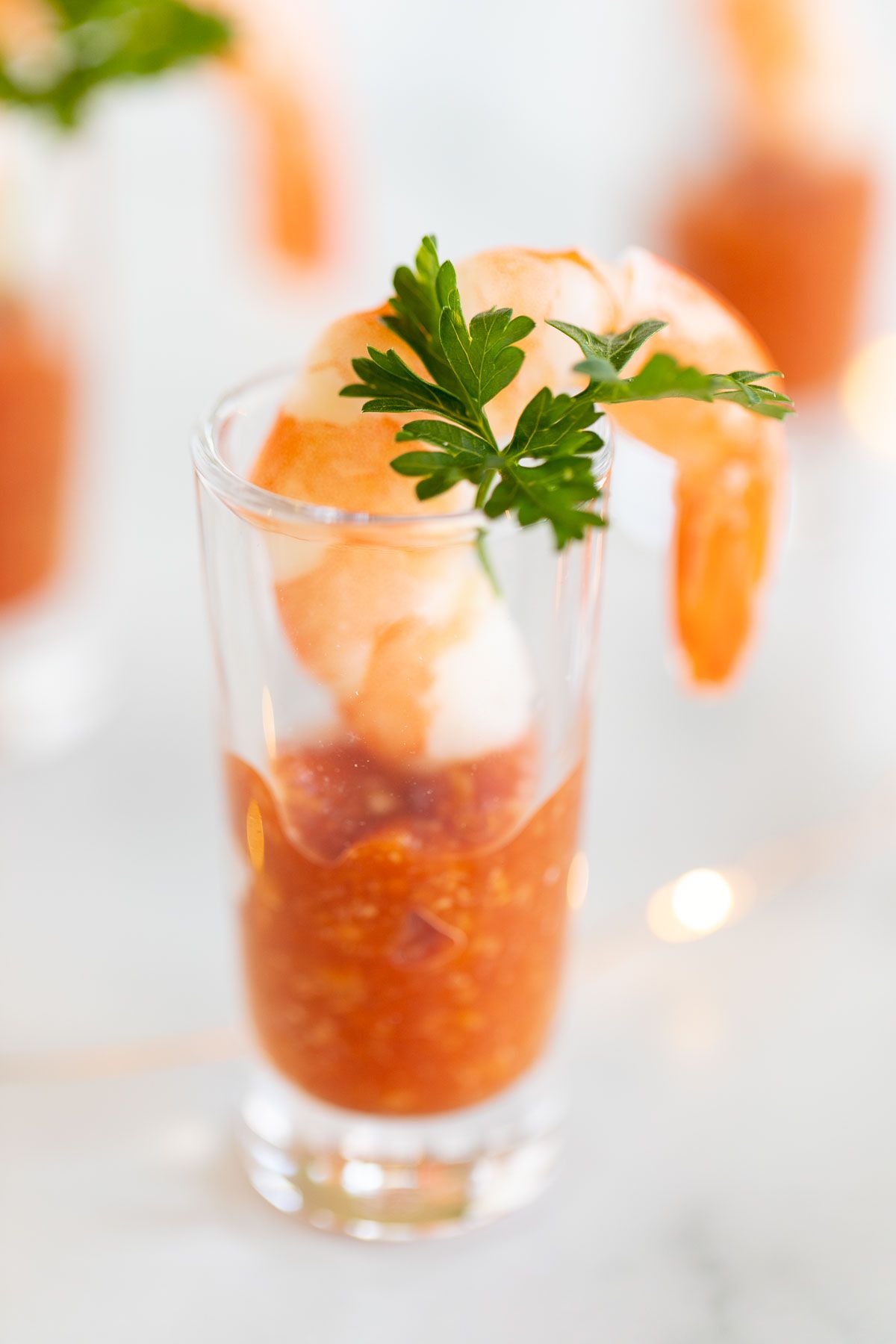 A small shot glass with the best cocktail sauce at the bottom, and a roasted shrimp hanging over the edge