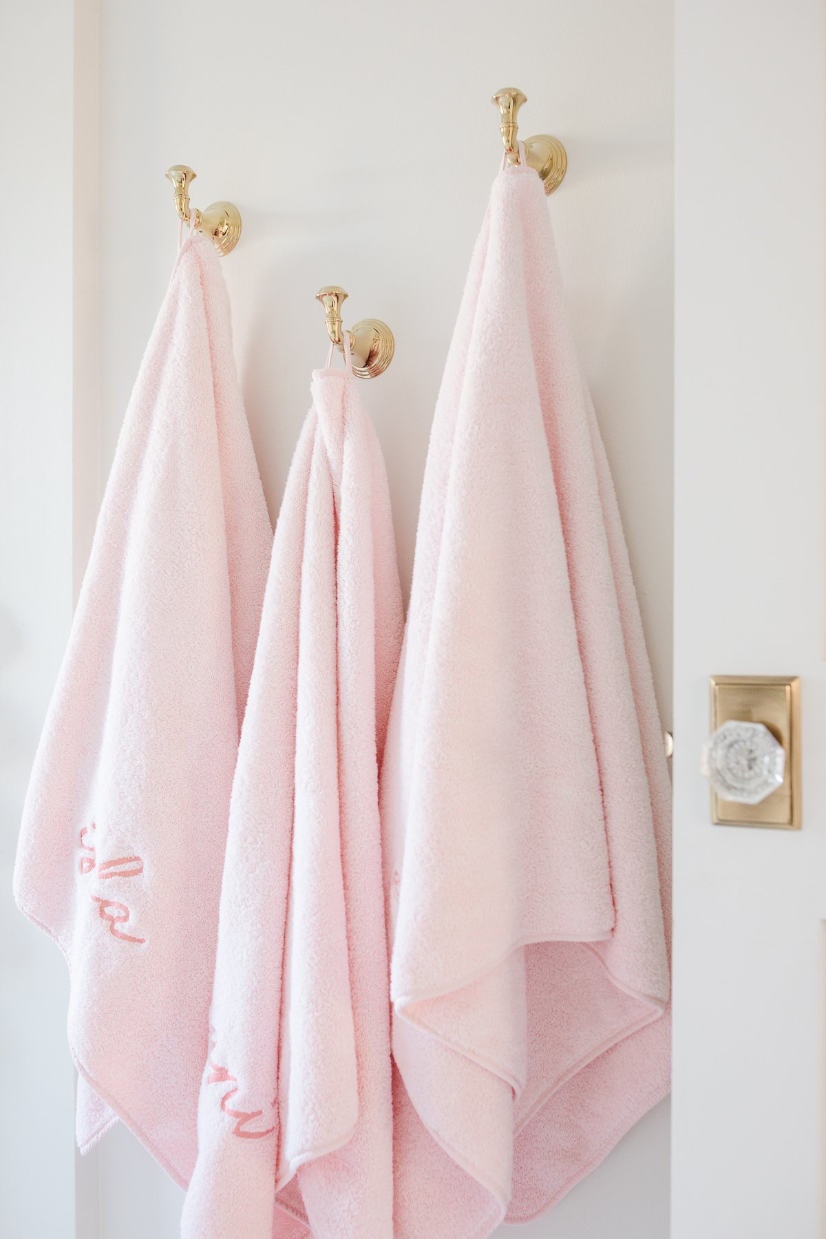 Pink towels hanging on brass hooks in a bathroom. 