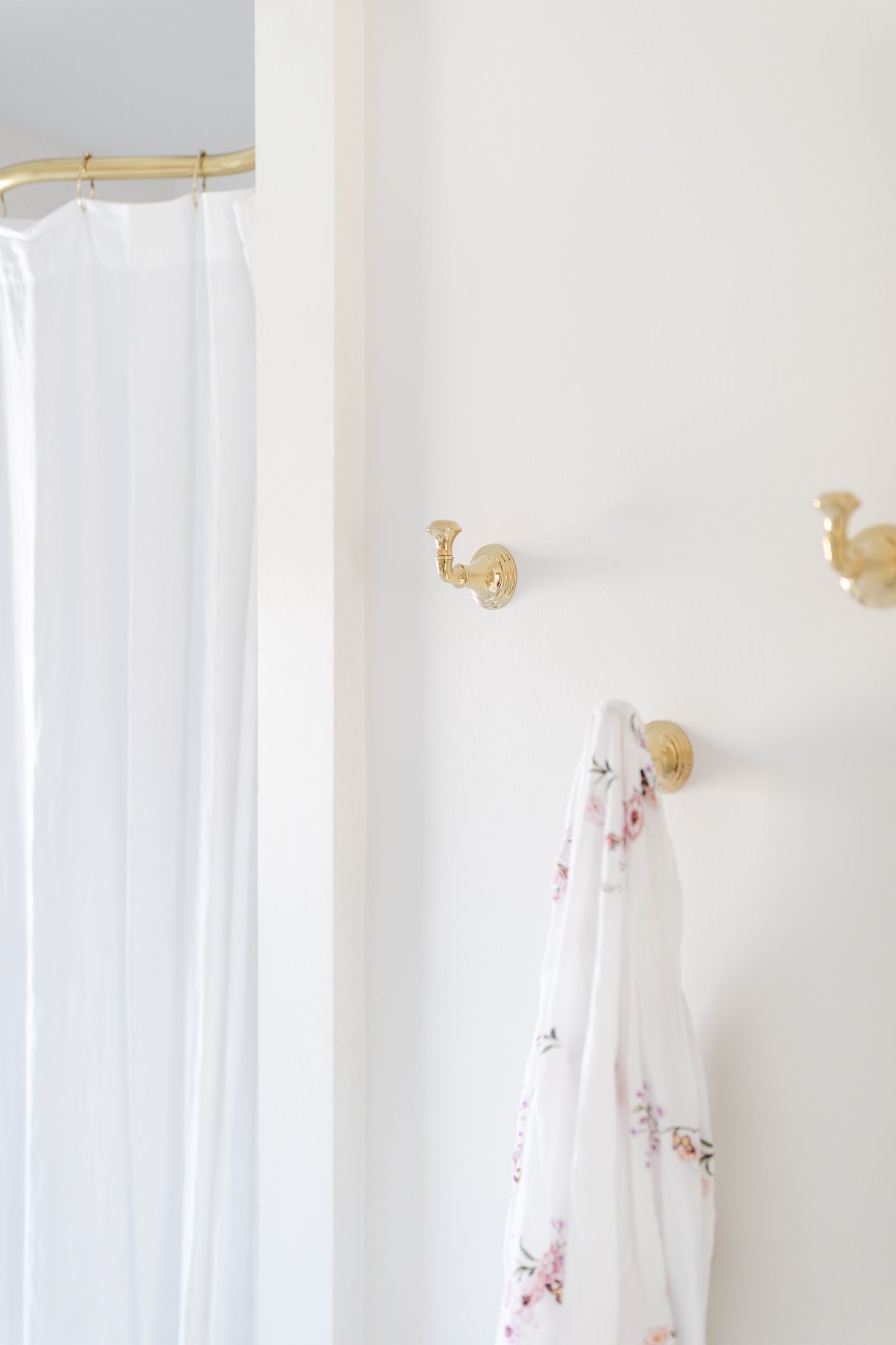 A white bathroom with brass hooks, a pink floral robe hanging from one.