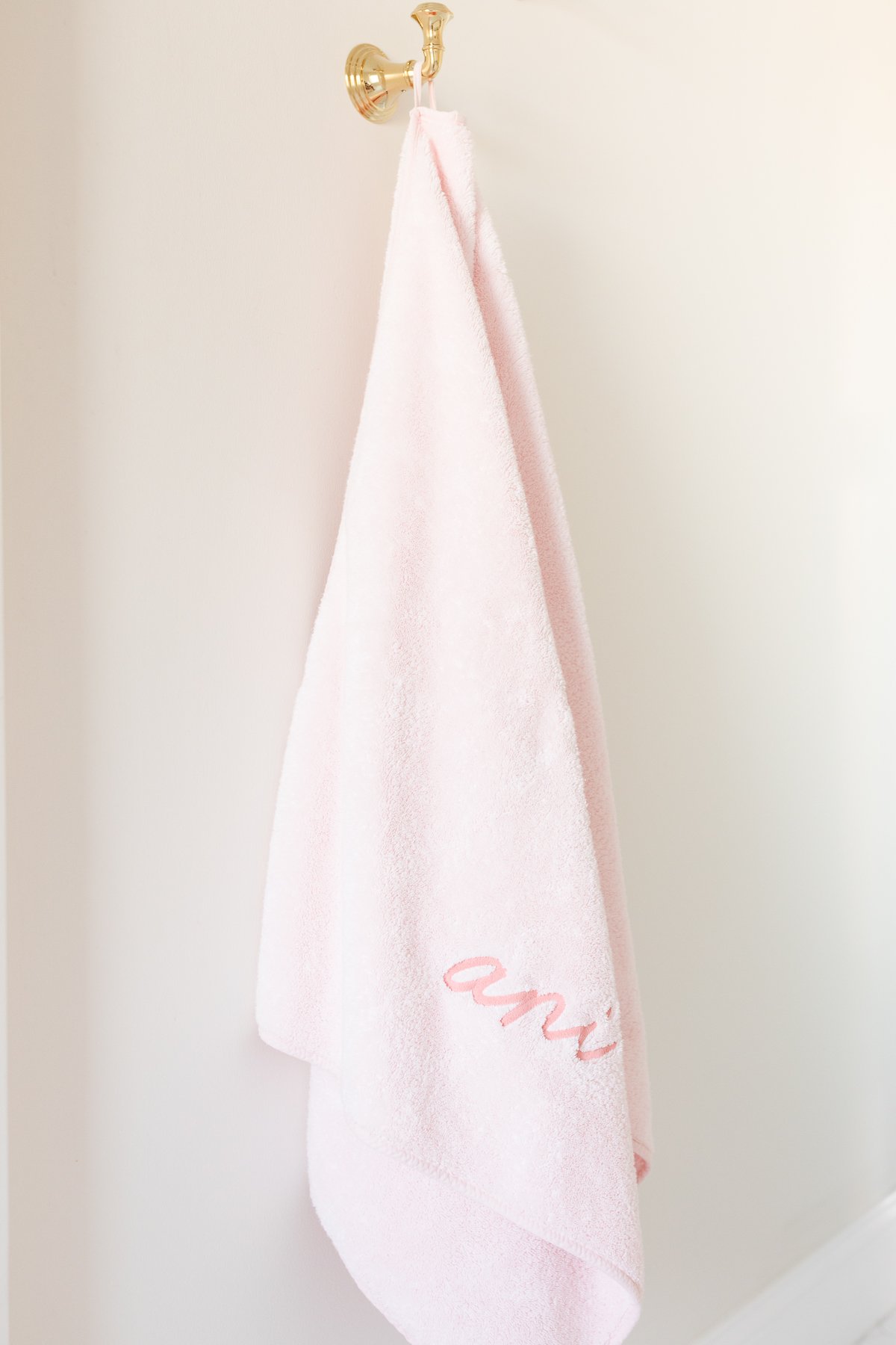 Pink towel hanging on a brass hook in a bathroom.