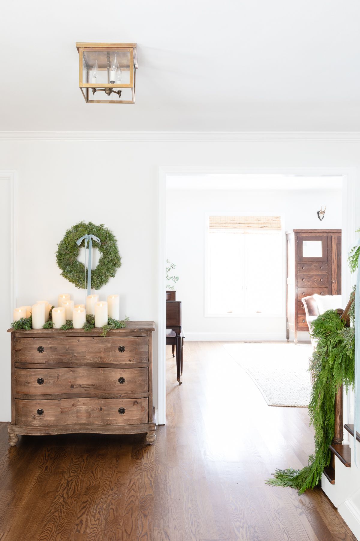 Entryway with fresh cedar wreath on staircase and flower wreath on chest of drawers.