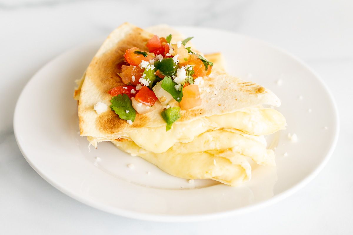 Cheese quesadilla sliced and stacked on a white plate, topped with pico de gallo