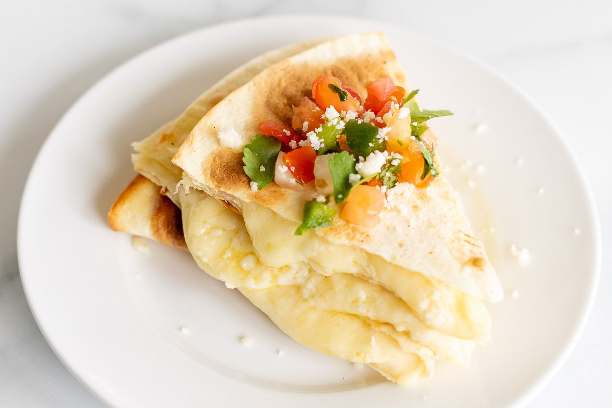 Cheese quesadilla sliced and stacked on a white plate, topped with pico de gallo