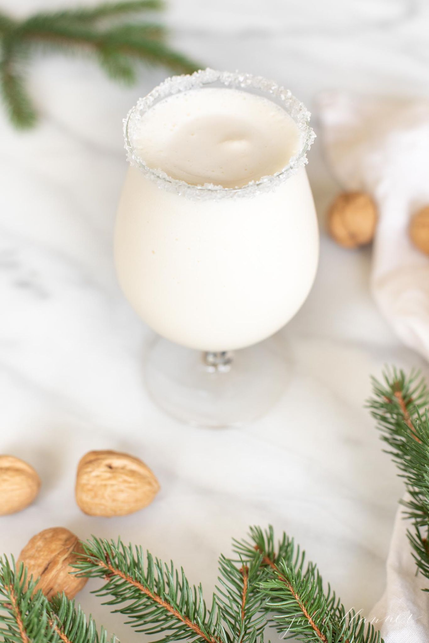 A clear stemmed glass filled with a white Christmas cocktail, topped with a marshmallow and a sugared rim.