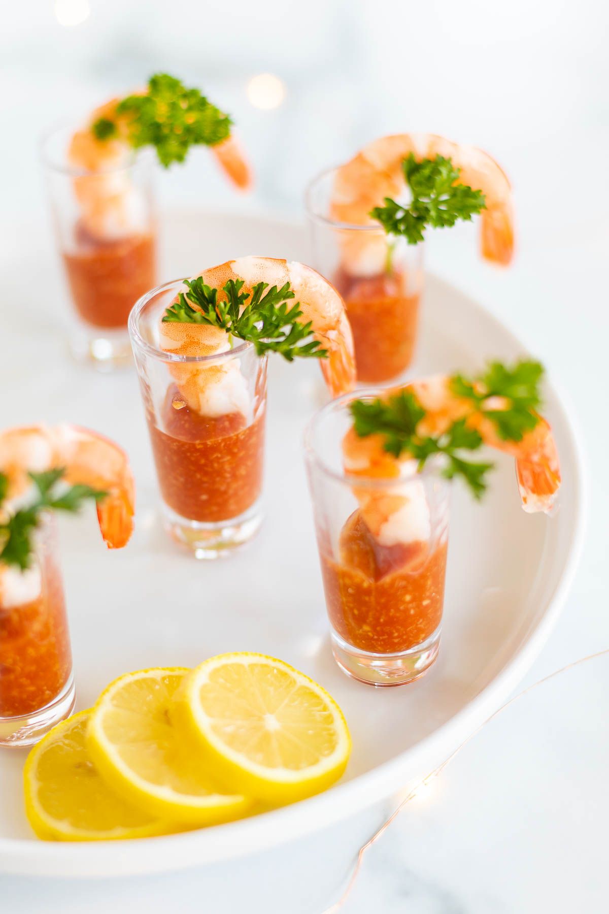 A round white tray with shot glasses featuring shrimp cocktail