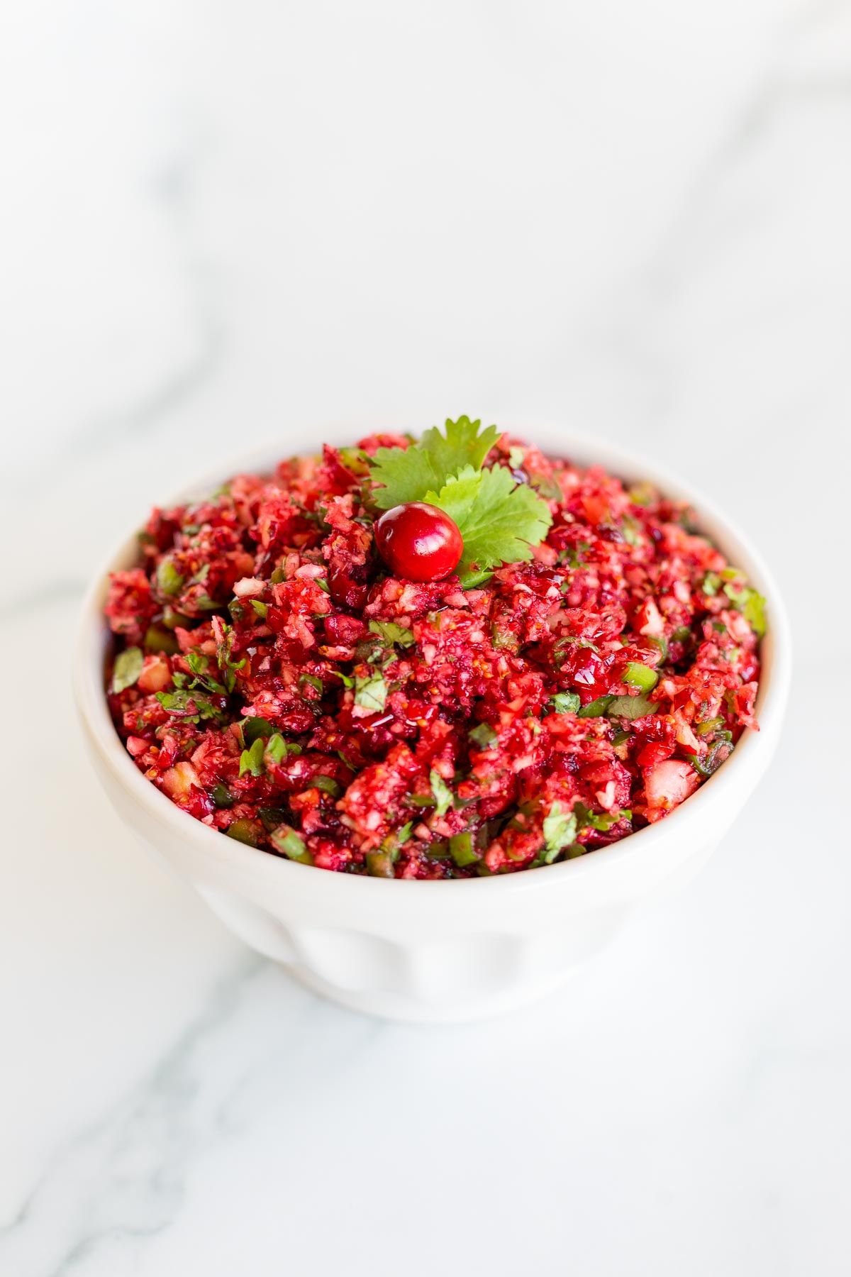 A white bowl full of cranberry salsa on a marble surface