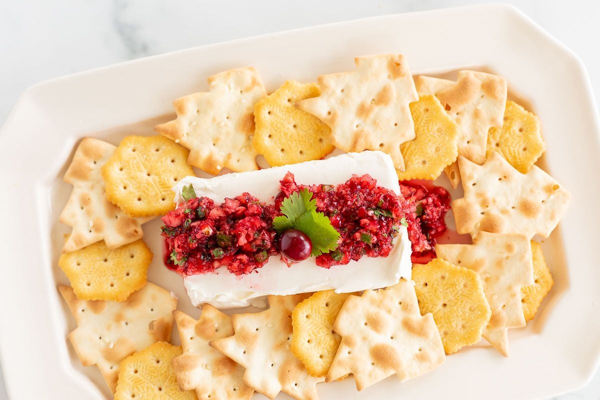 A platter of crackers surrounding cranberry salsa on a block of cream cheese