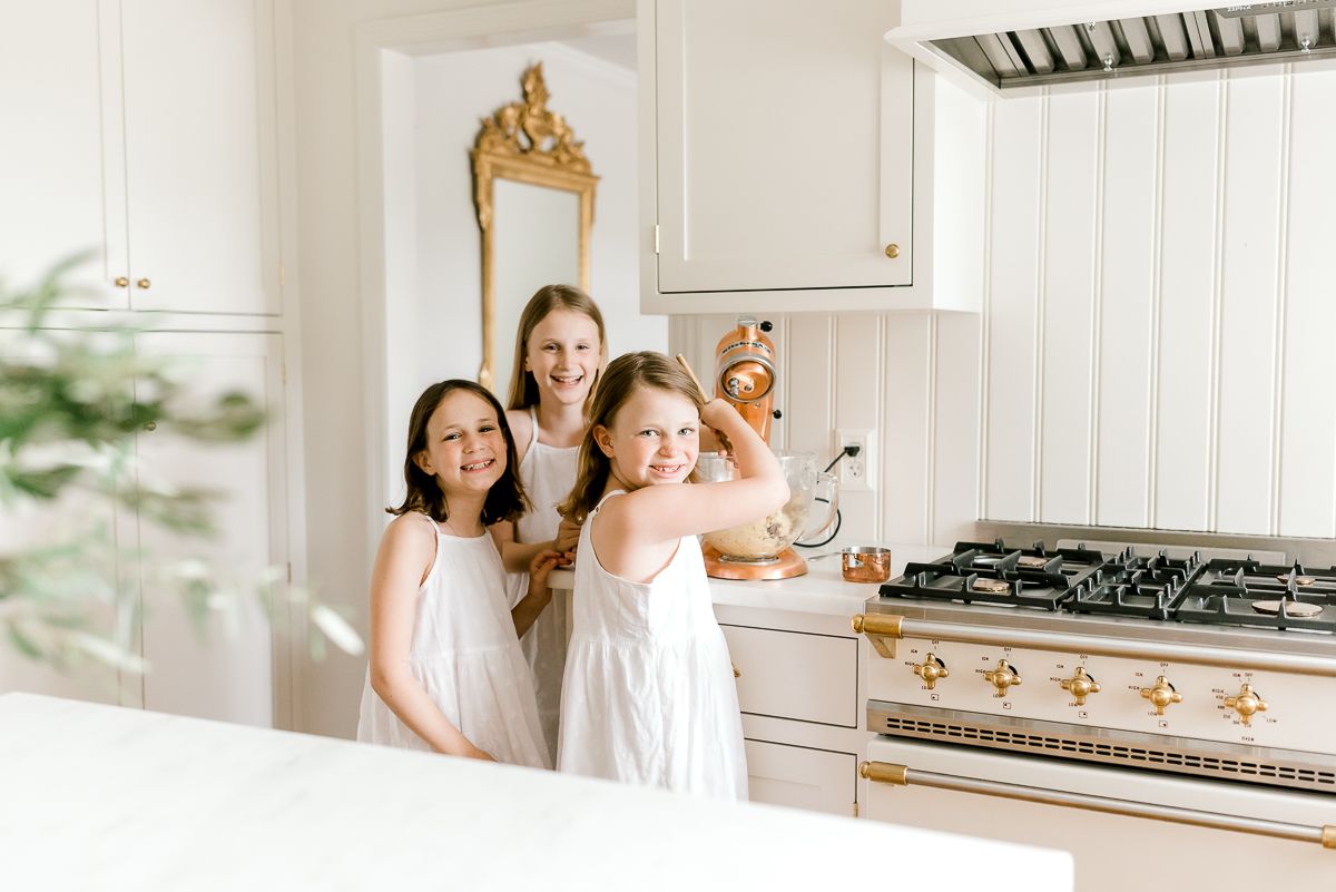 Three little girls in white dresses in a white kitchen