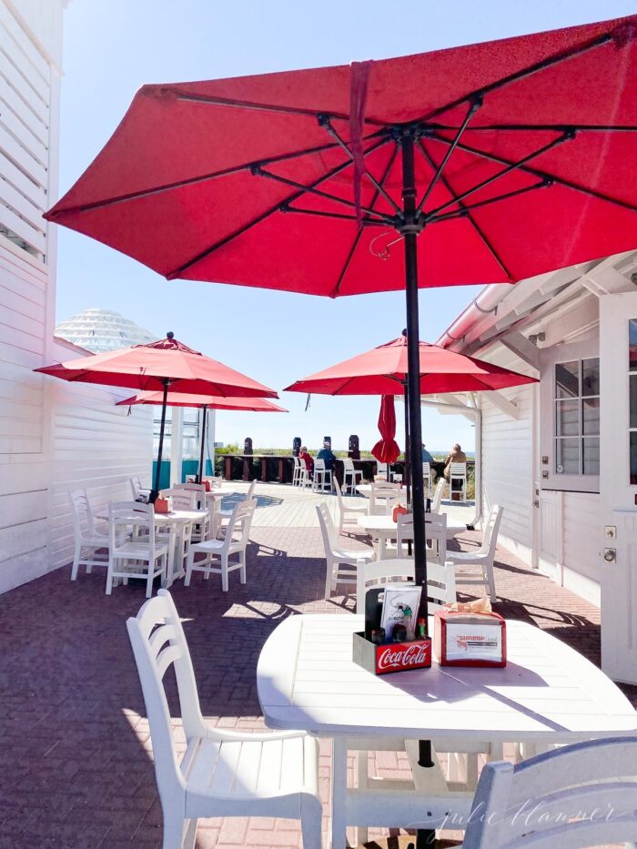 An outdoor restaurant patio with white tables and red umbrellas