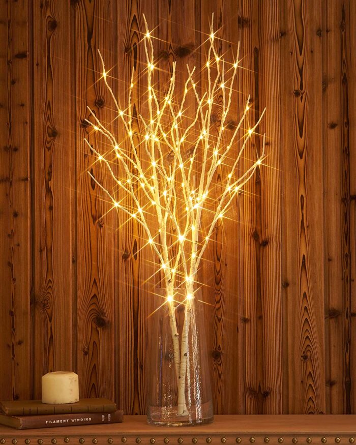 lighted birch branches in a vase with a wood paneling background