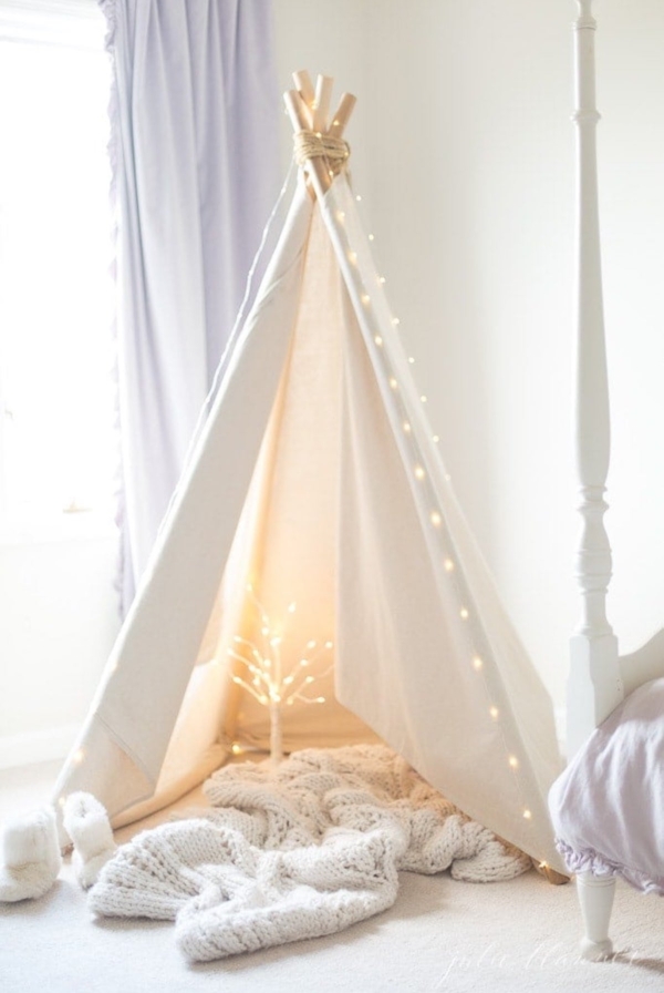 A white teepee adorned with fairy lights in a bedroom.