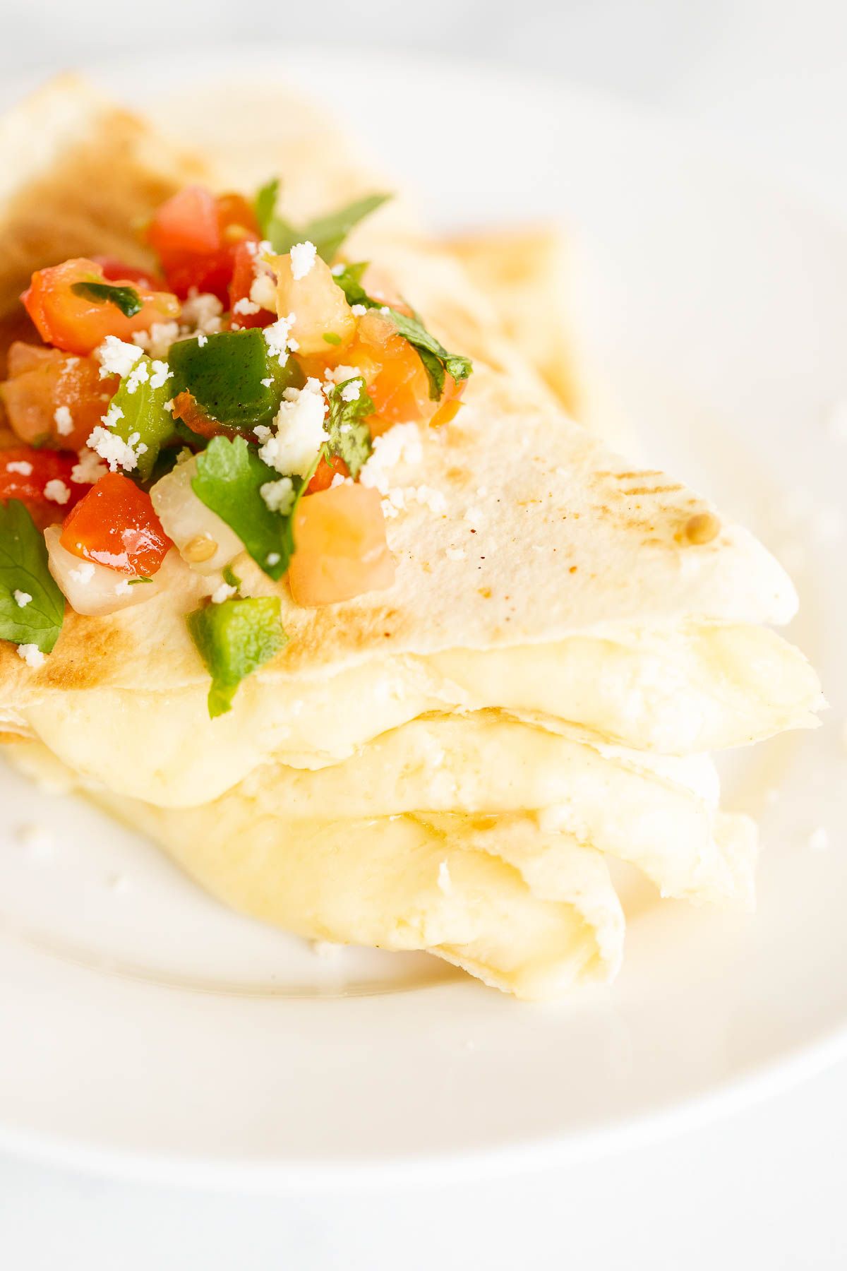 Cheese quesadilla sliced and stacked on a white plate, topped with pico de gallo