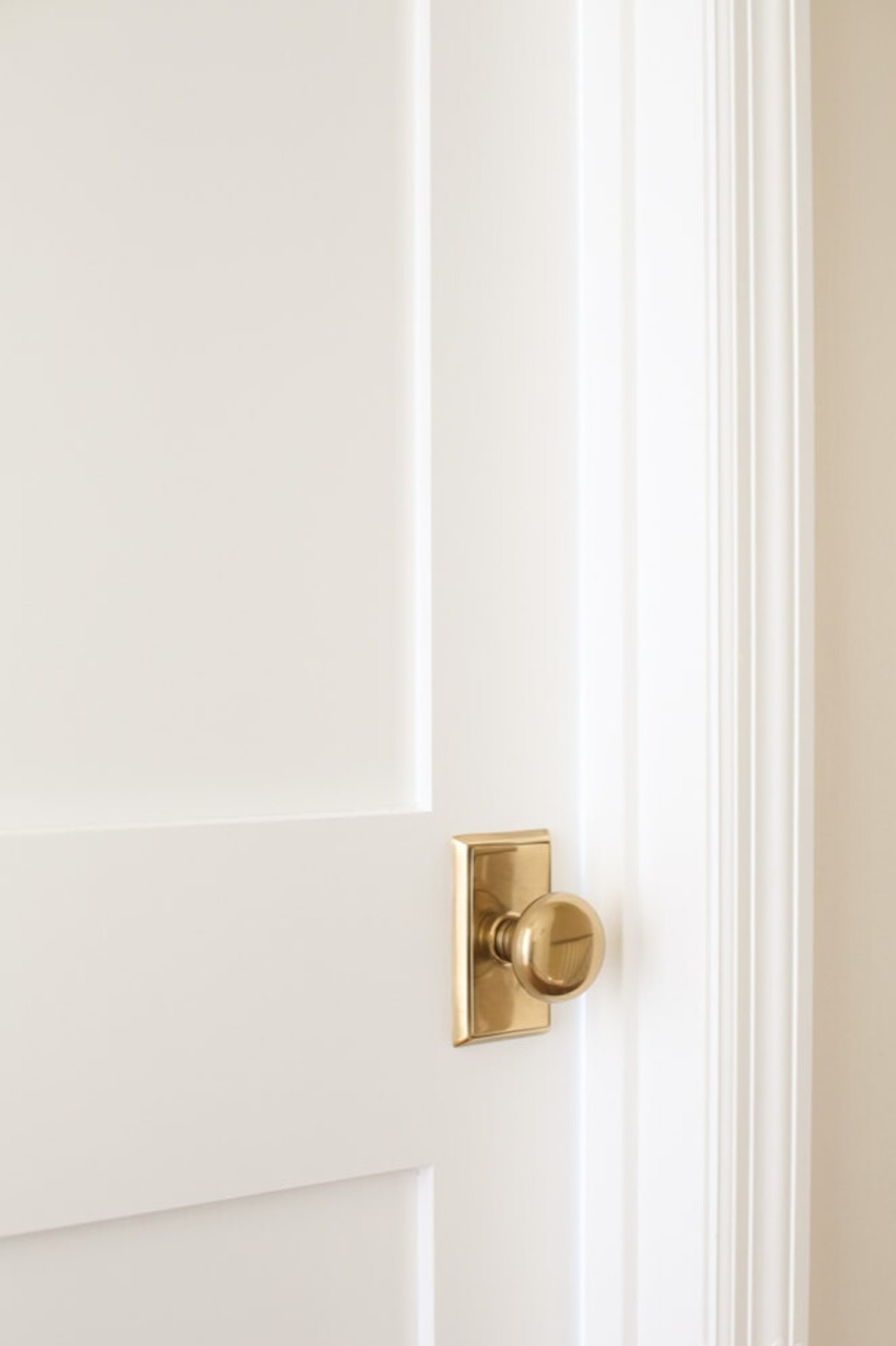 A white door partially ajar with a brass knob and trim, freshly painted for an interior makeover.