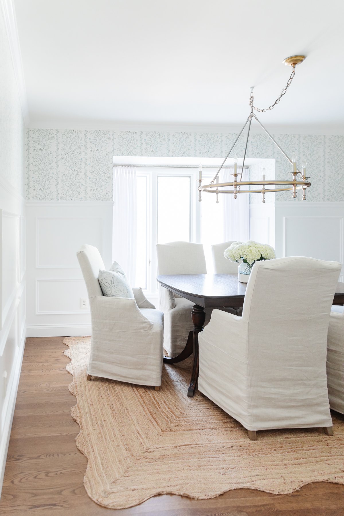 A dining room with neutral rugs and white chairs.