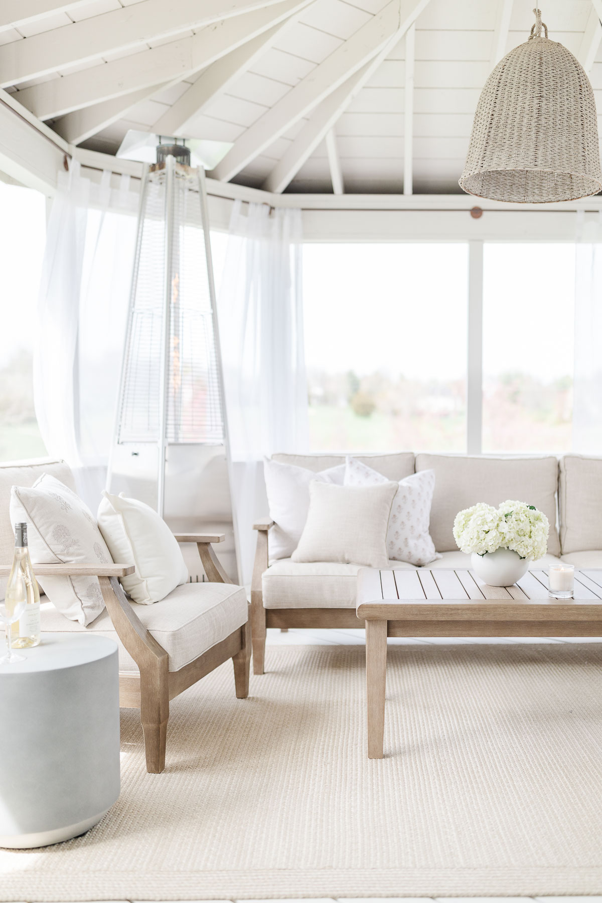 A screened in porch with white furniture and a coffee table, adorned with neutral rugs.