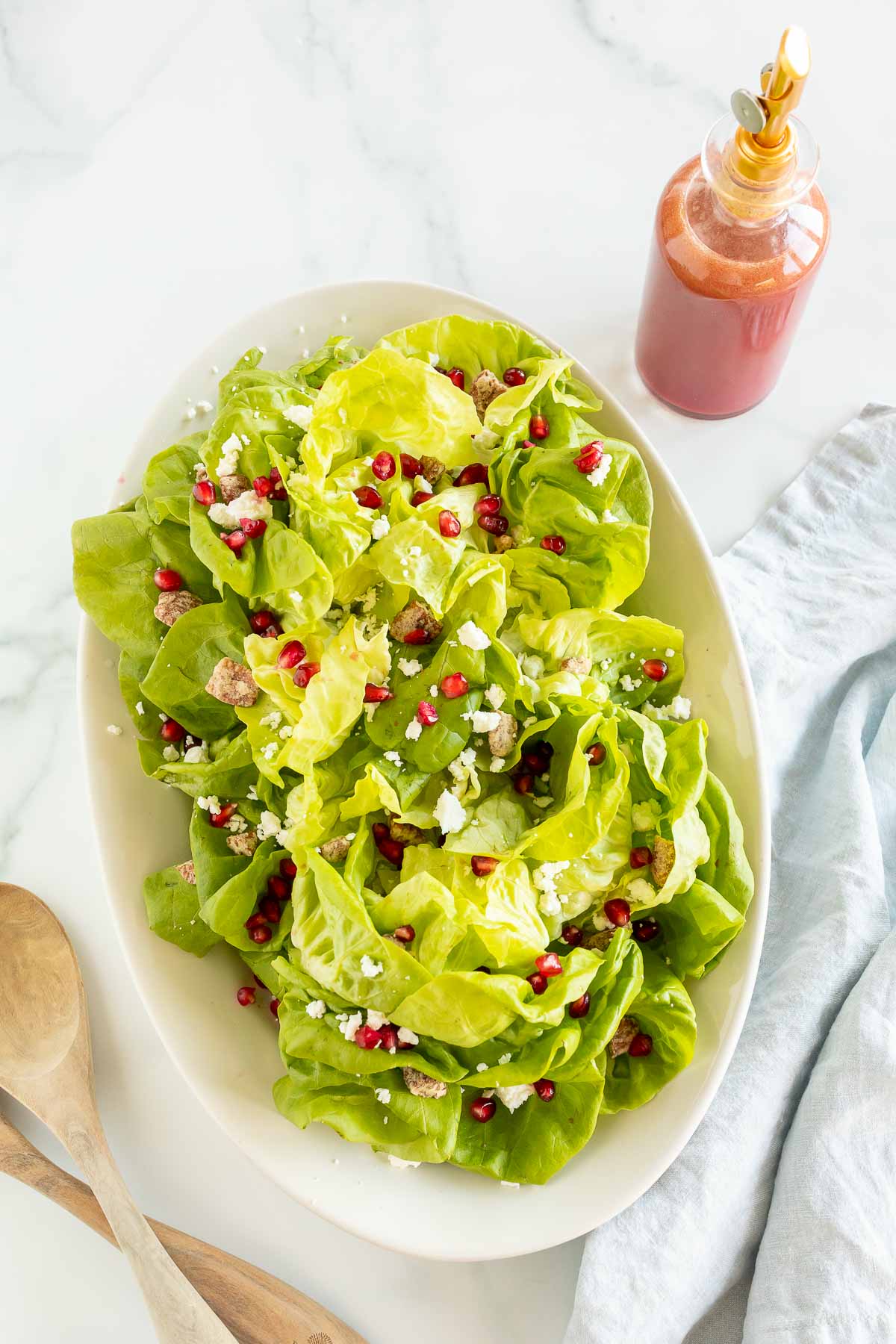 pomegranate salad on a platter with dressing next and wood servers
