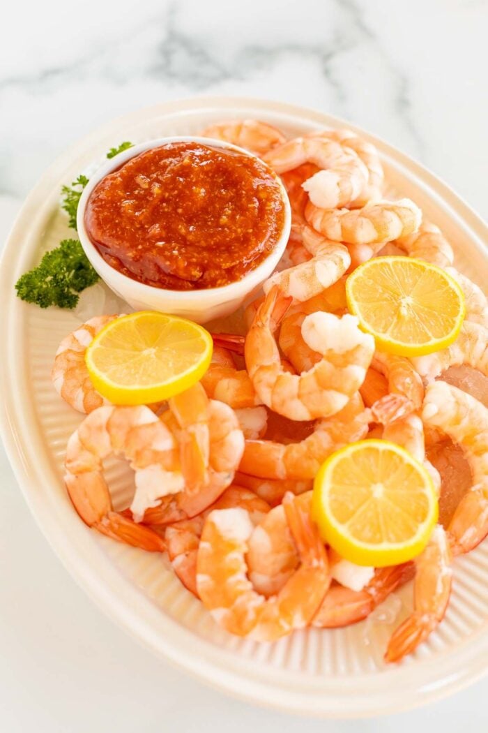 Eine ovale Platte mit gerösteten Shrimps-Cocktails mit einer hausgemachten Cocktailsauce in einer weißen Schüssel.