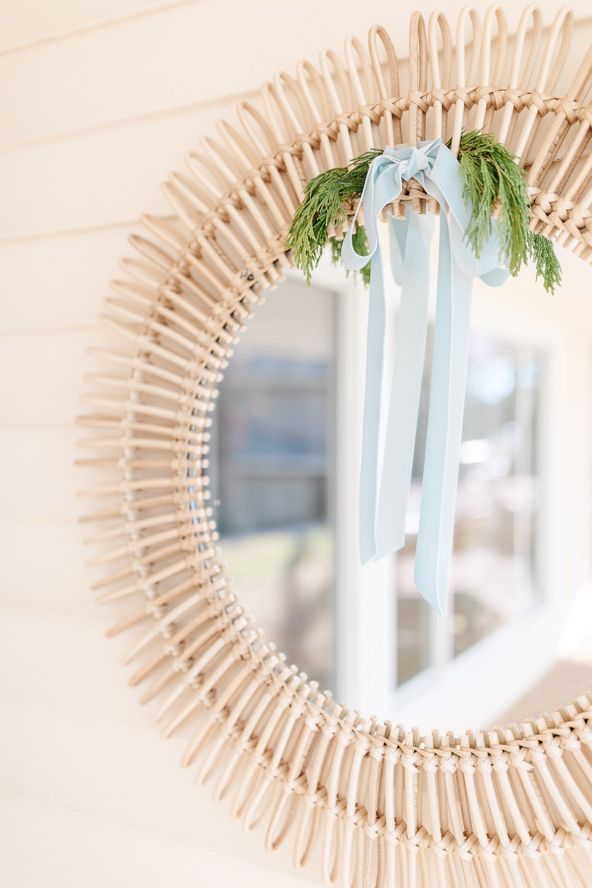 A round rattan mirror with a blue ribbon and greenery tied on