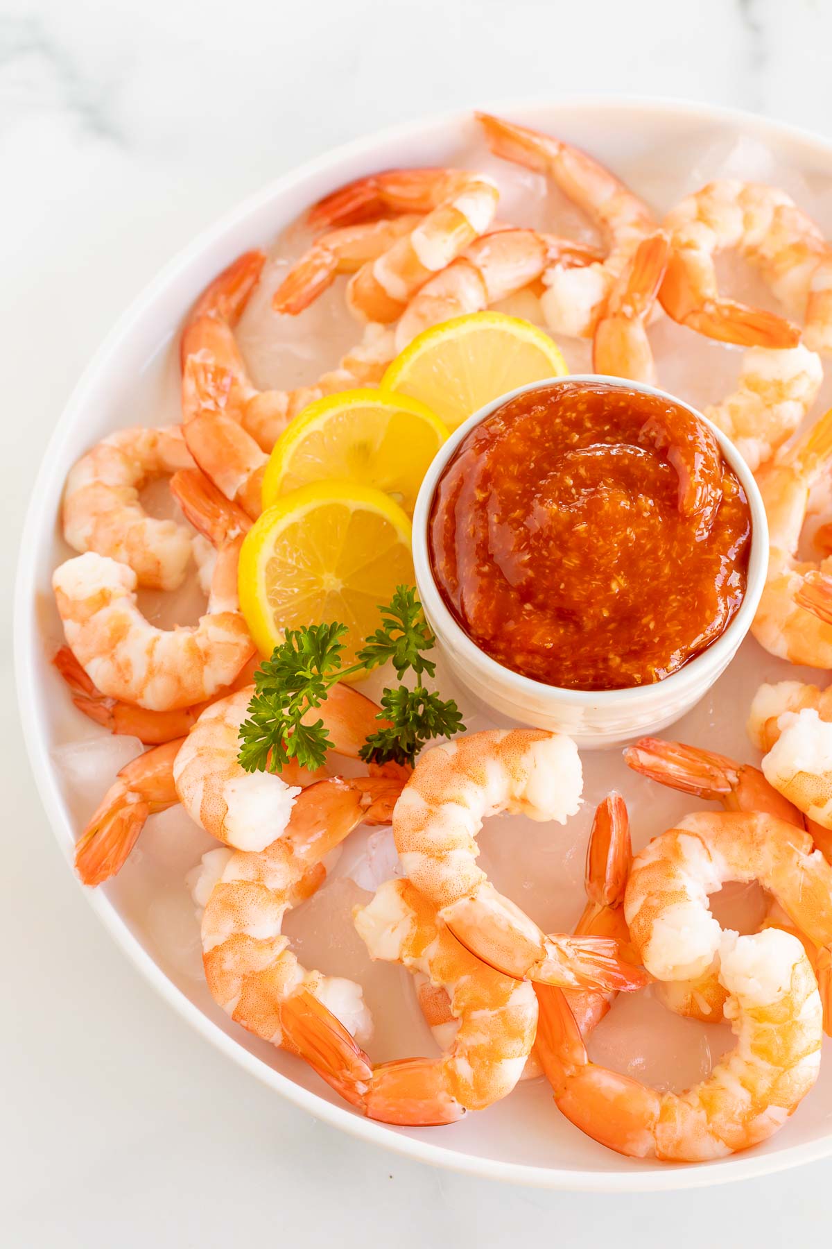 An oval platter of roasted shrimp cocktail with a homemade cocktail sauce in a white bowl.