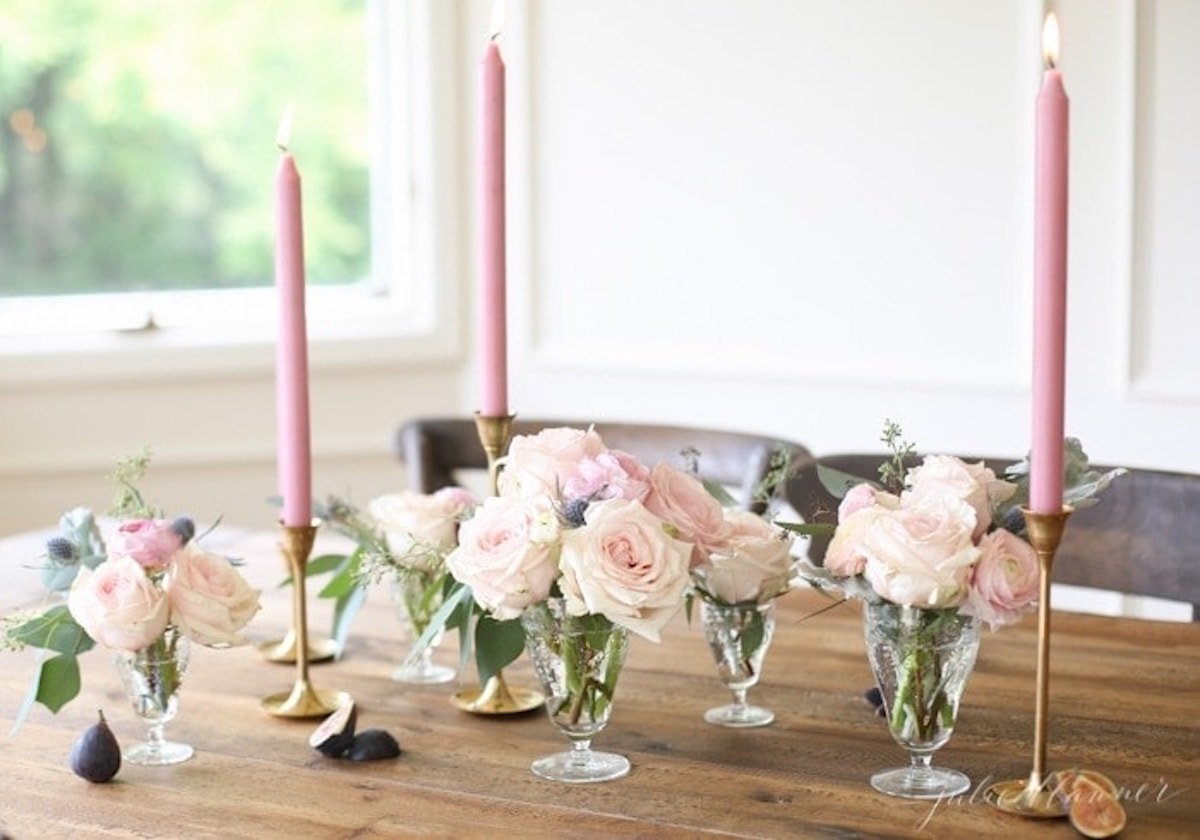 Pink roses and candles create a beautiful Thanksgiving table centerpiece on a wooden table.