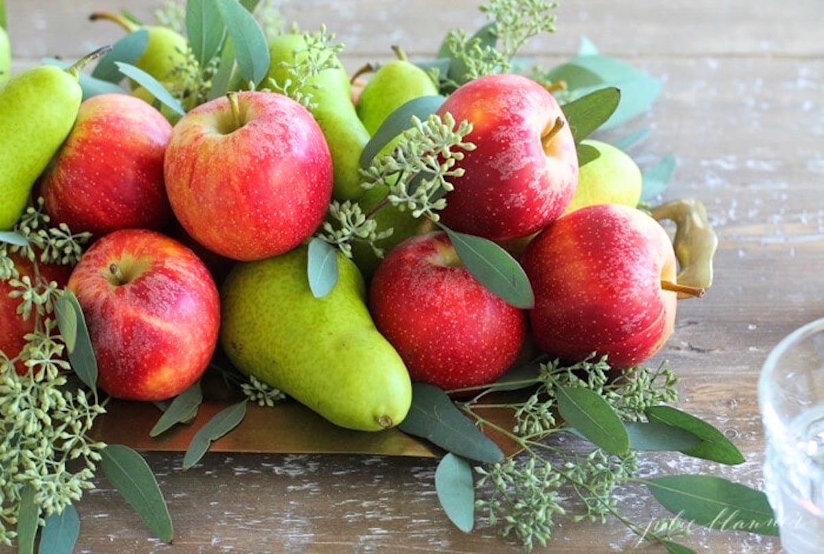 A festive Thanksgiving table centerpiece featuring an arrangement of apples, pears, and greenery.