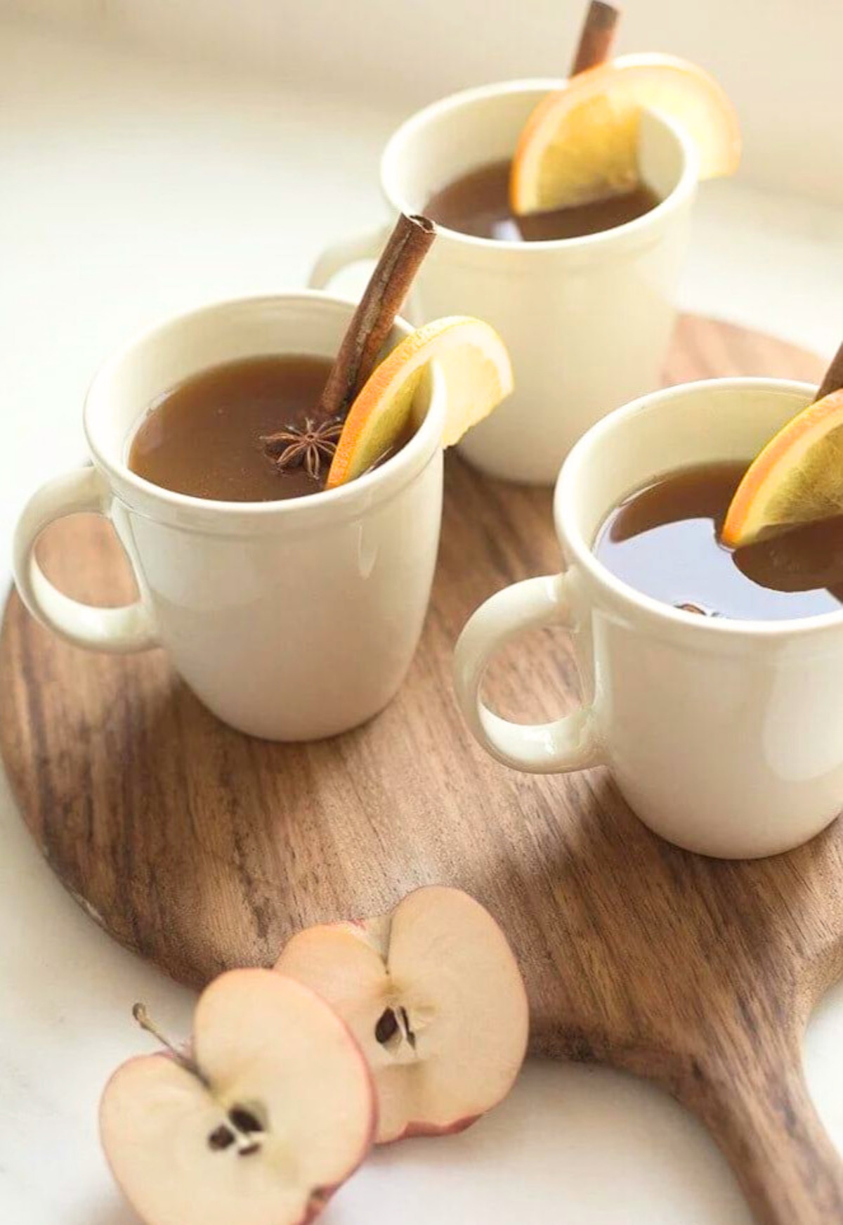 Three mugs of apple cider with cinnamon sticks, perfect for Thanksgiving cocktails or drinks.
