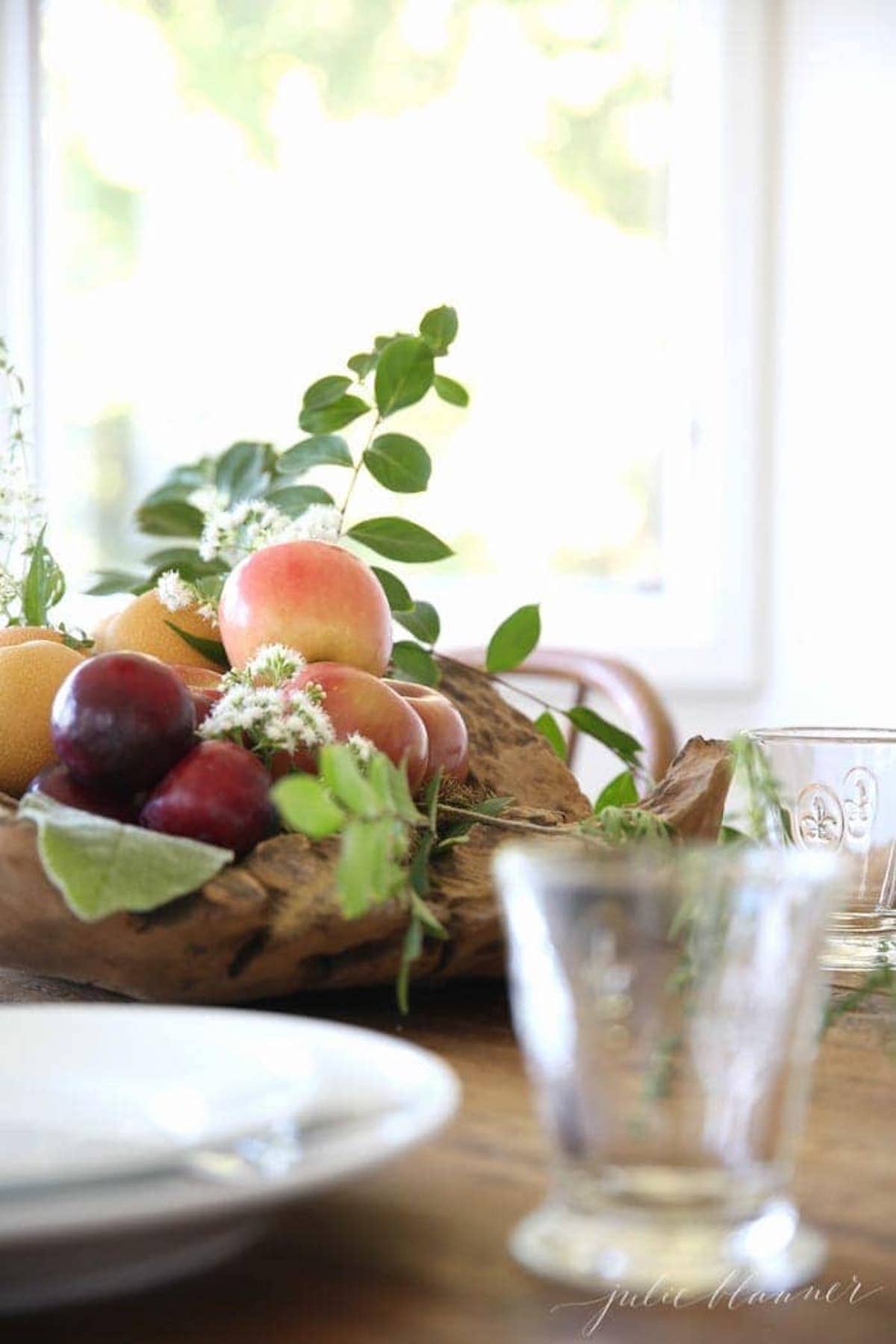 A festive Thanksgiving centerpiece featuring a wooden bowl brimming with an assortment of fresh fruit and vibrant greenery, adorning the holiday table.