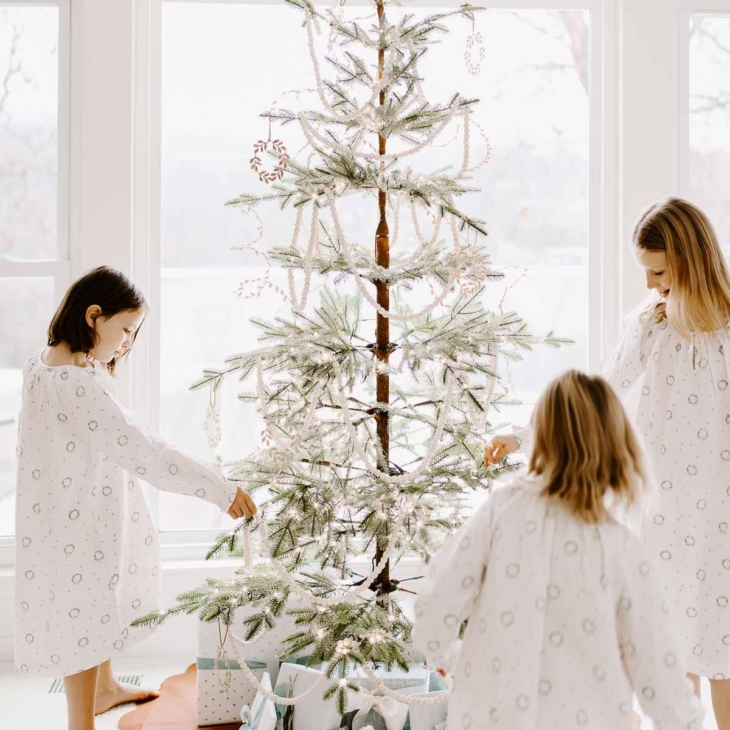 Three little girls surrounding a Christmas tree in a white living room