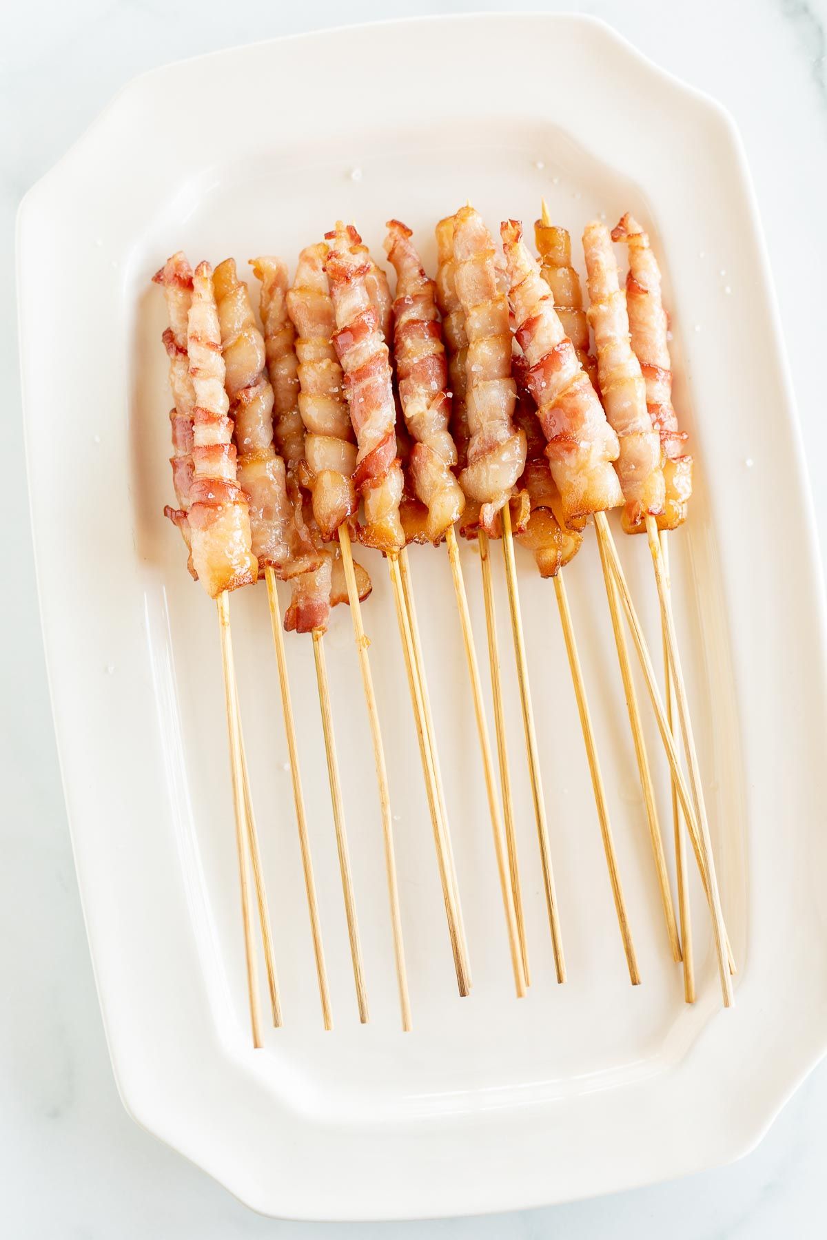 Caramelized bacon skewers on a white platter.