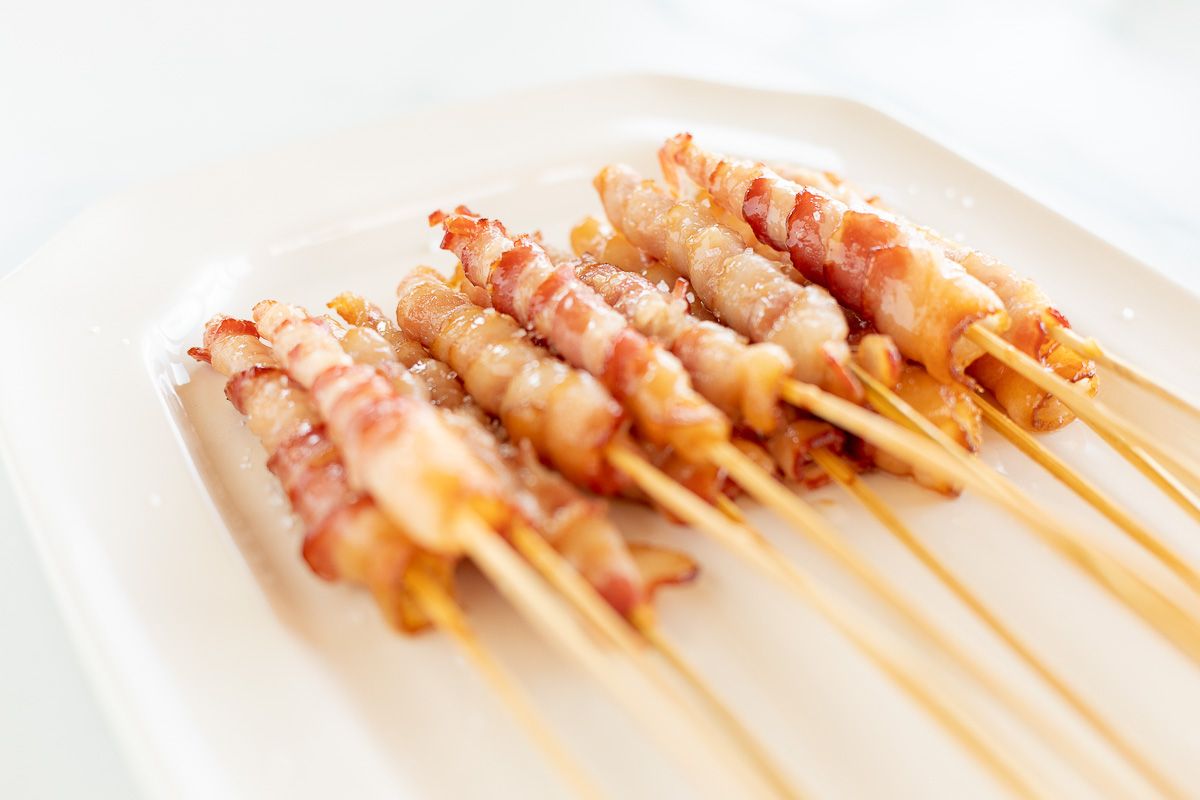 Caramelized bacon skewers on a white platter.