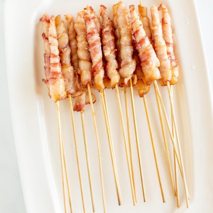 Caramelized bacon skewers on a white platter