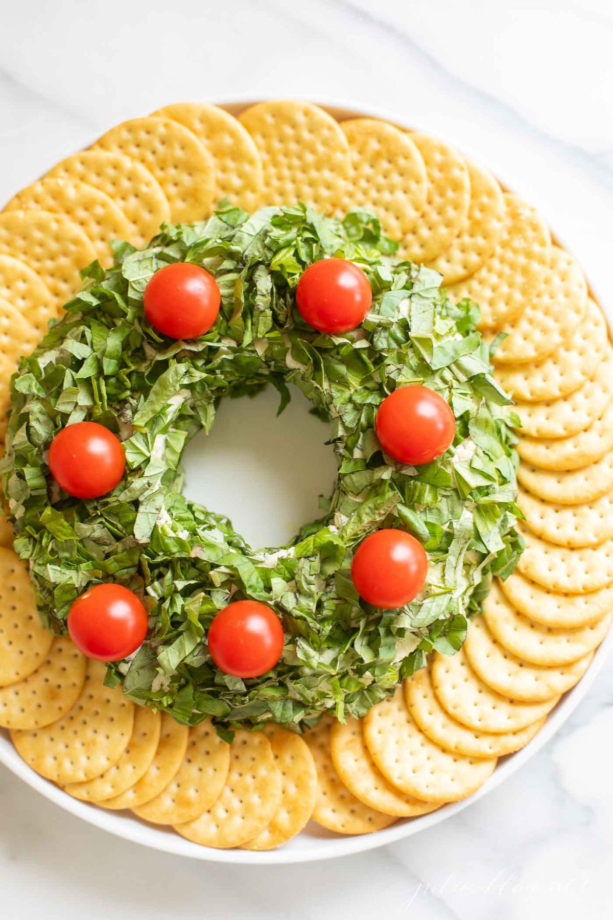 a pesto cheeseball wreath for a Christmas appetizer, surrounded by crackers on a white platter