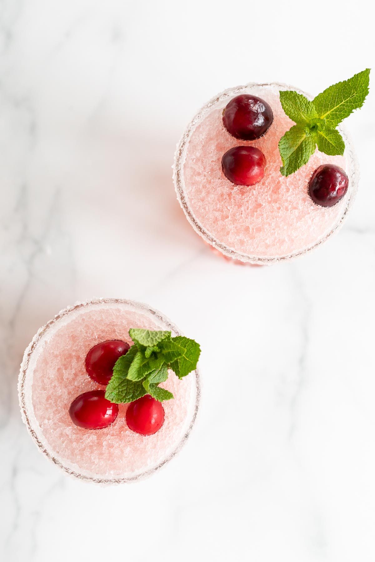A pair of cranberry margaritas topped with fresh cranberries and mint