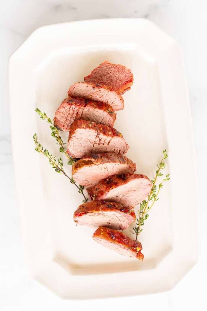 Grilled beef tenderloin on a white platter, garnished with fresh thyme.