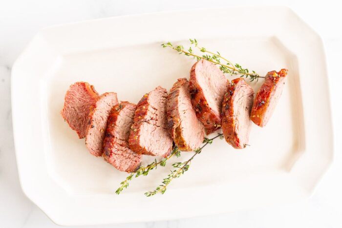 Grilled beef tenderloin on a white platter, garnished with fresh thyme.