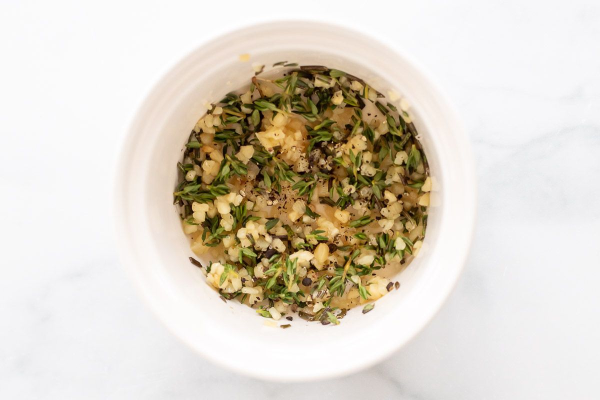 A white bowl full of fresh chopped herbs, minced garlic