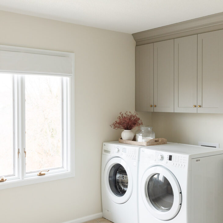 neutral laundry room with gray cabinets and brass light