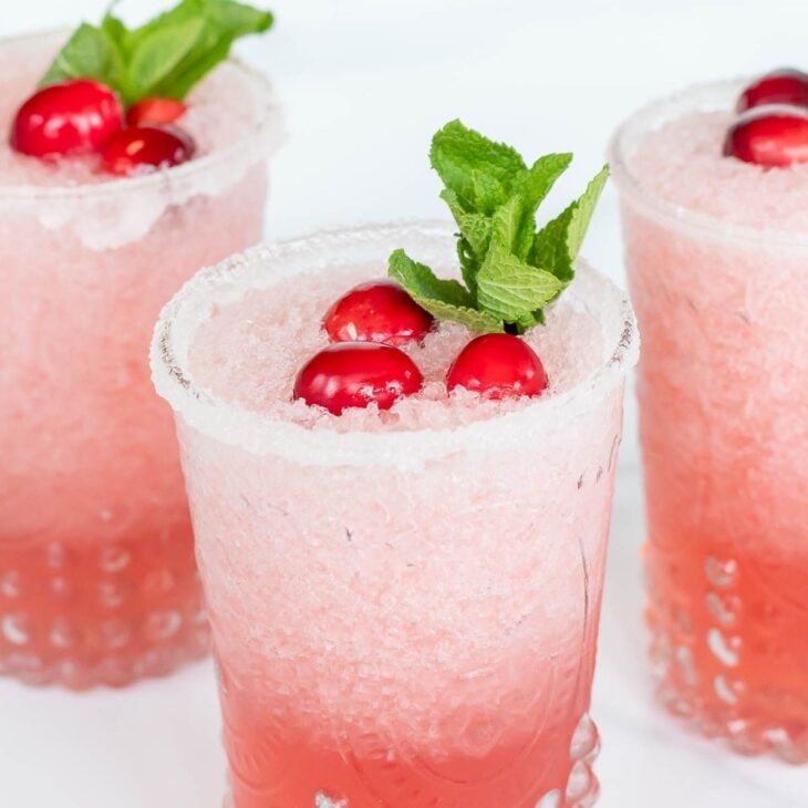Pretty clear glasses full of Mistletoe Margaritas, topped with fresh mint and cranberries.