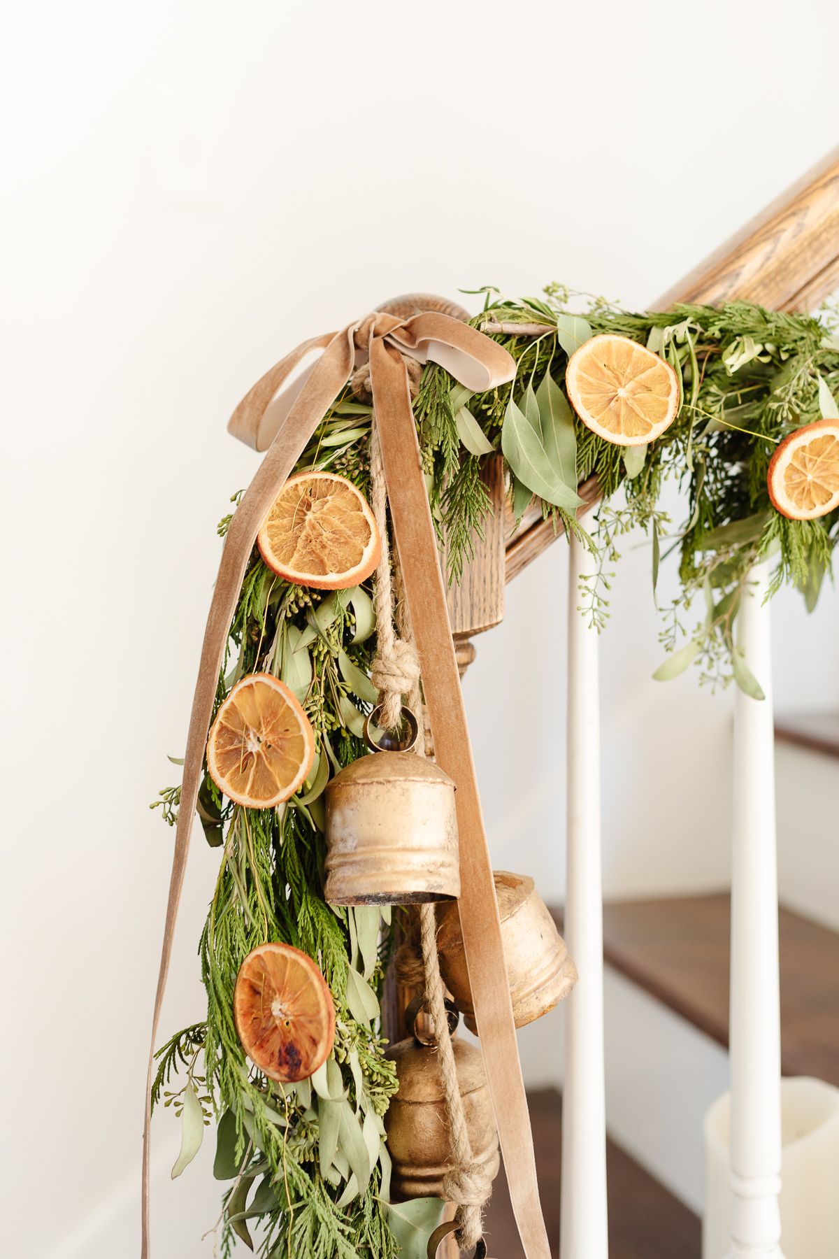 An orange garland on a staircase with evergreen garland, velvet ribbon and brass bells.