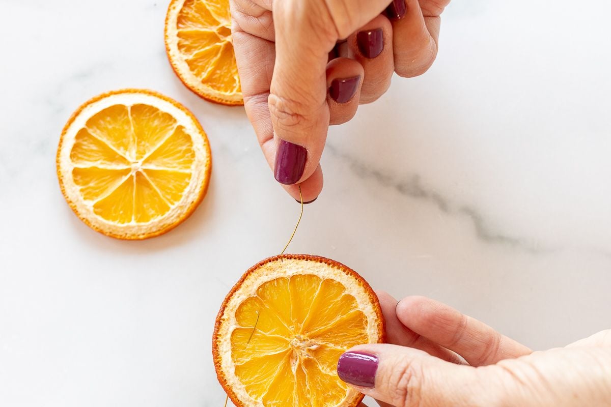 A woman's hands stringing an orange garland on a marble surface.