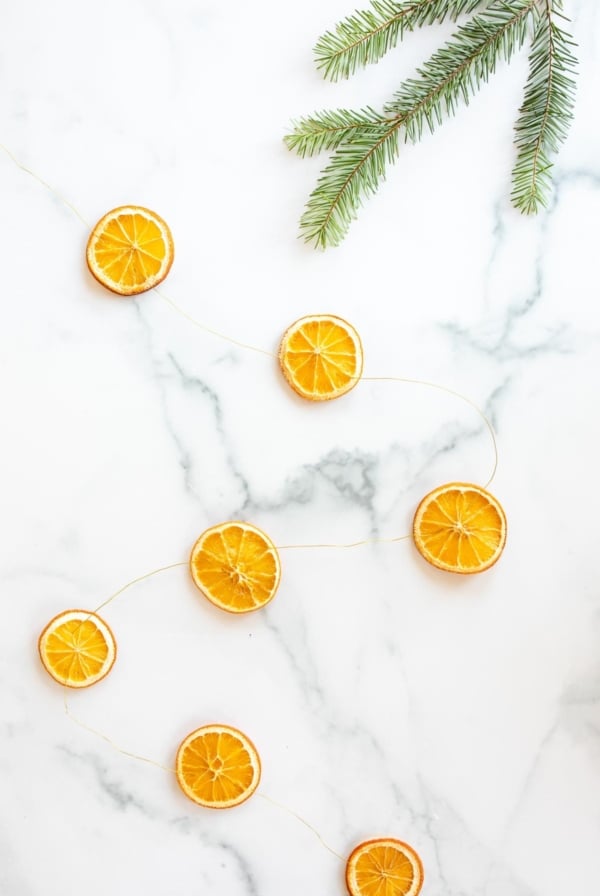 An orange garland laid out on a marble surface with a piece of evergreen to the side.