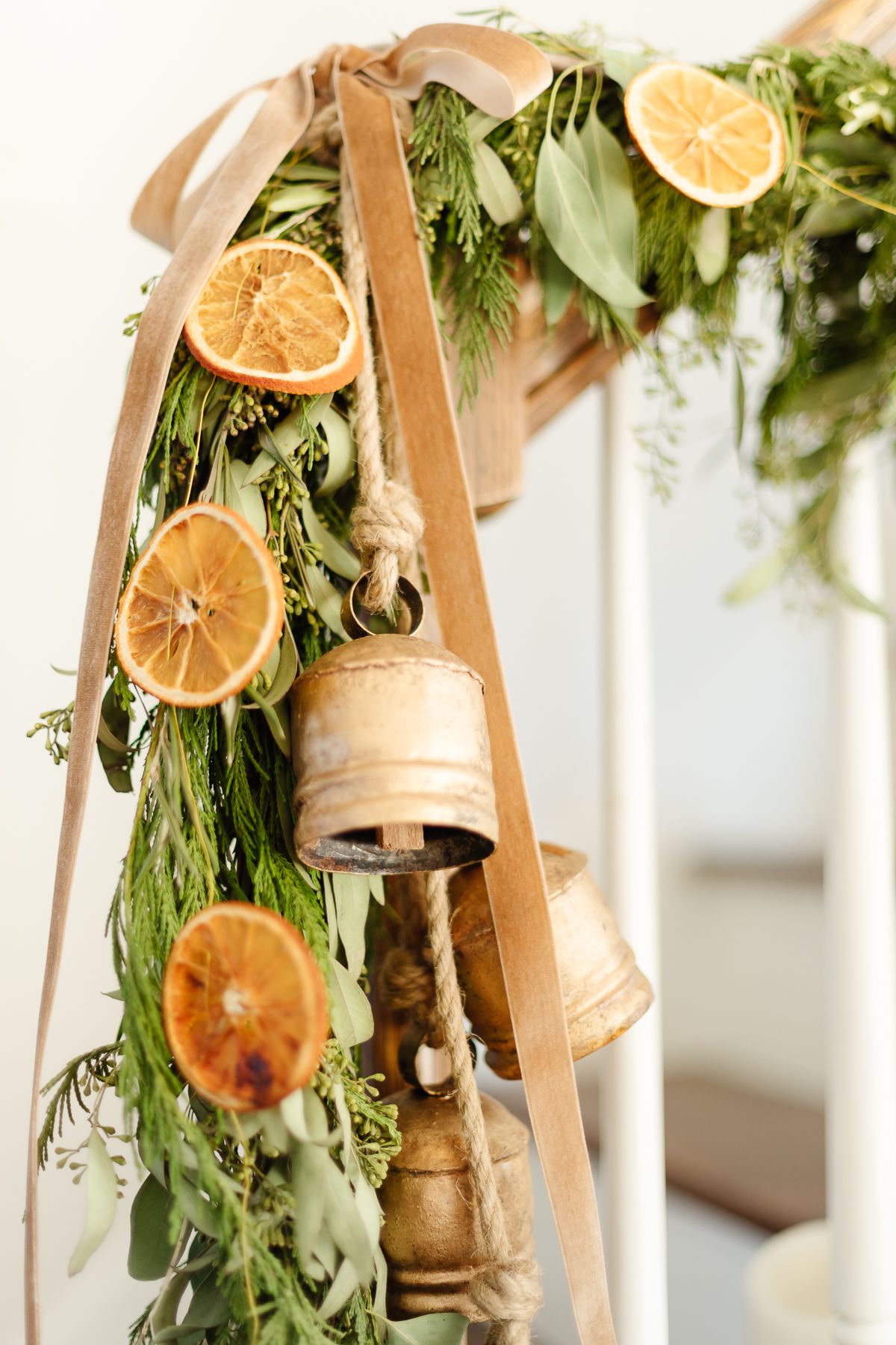 An orange garland on a staircase with evergreen garland, velvet ribbon and brass bells.